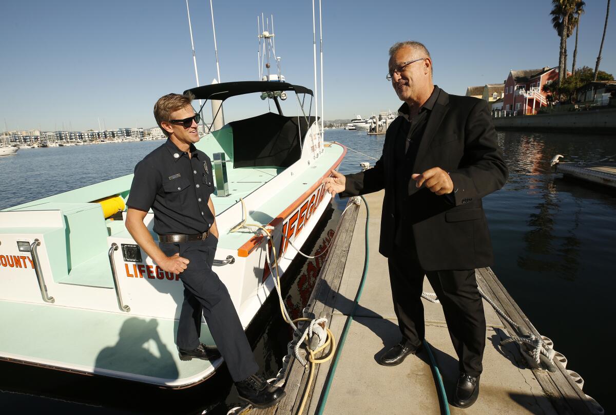 A man in a suit on a dock talks to a man in a ship's captain suit on a boat
