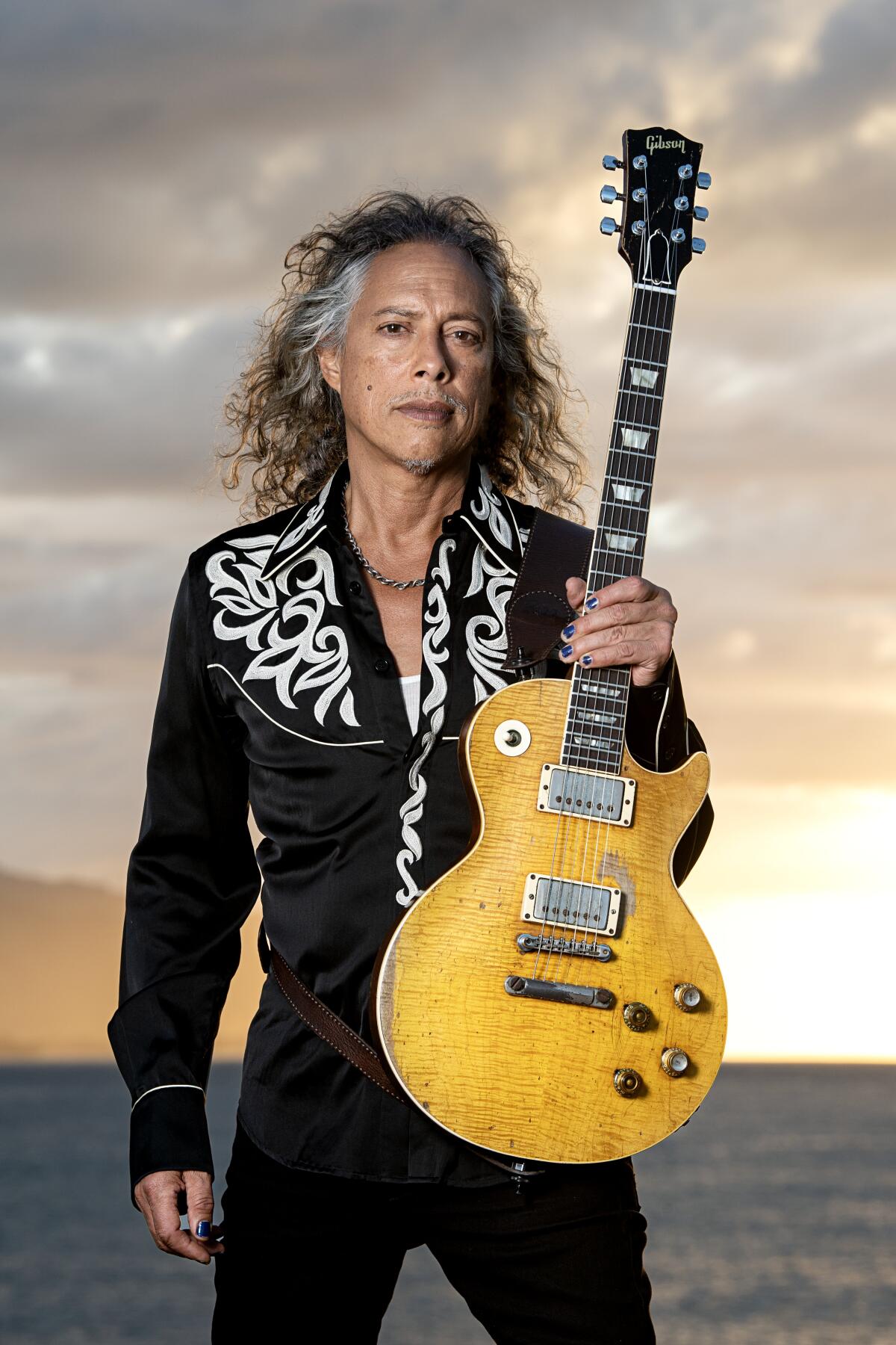 Kirk Hammett dressed in black holding a gold guitar