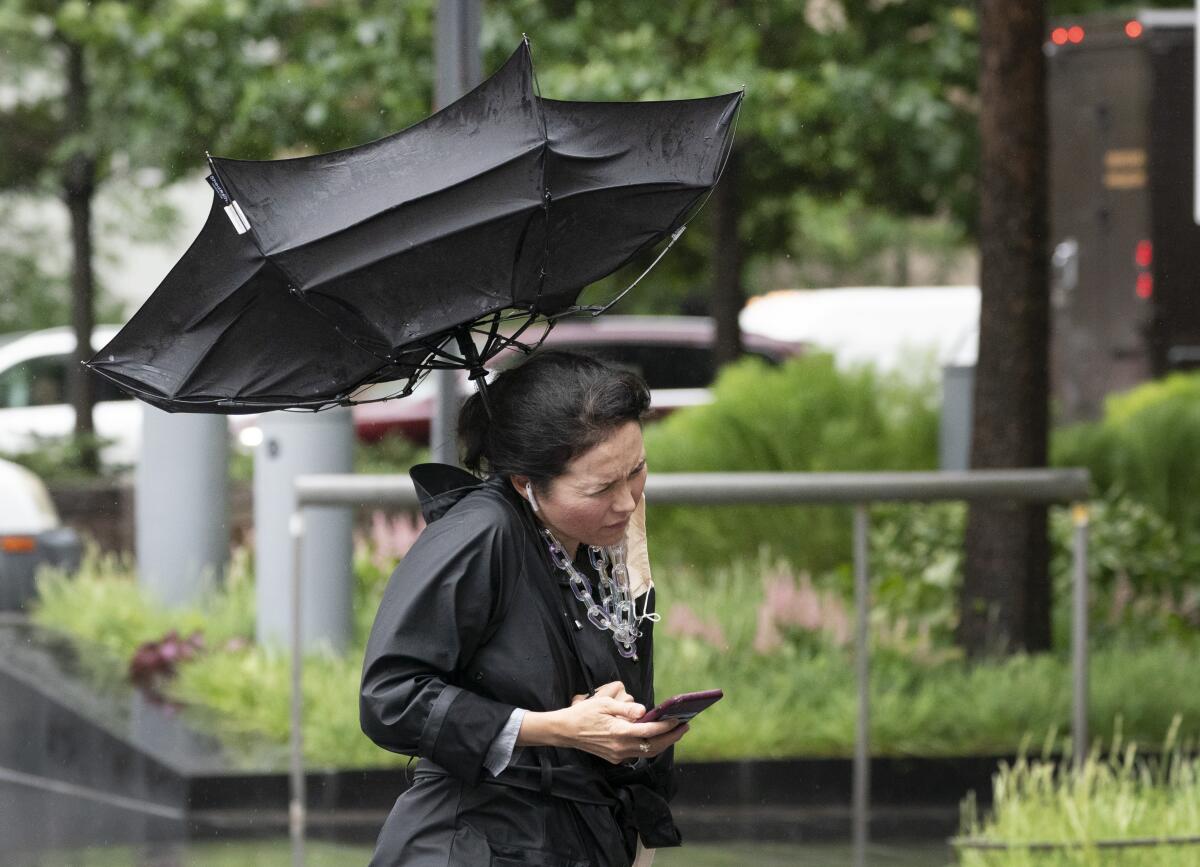 A woman's umbrella is flipped inside out as she walks on a rainy and windy New York street, Friday, July 9, 2021. Fast-moving Tropical Storm Elsa hit the New York City region with torrential rains and high winds as it churned up the East Coast. (AP Photo/Mark Lennihan)