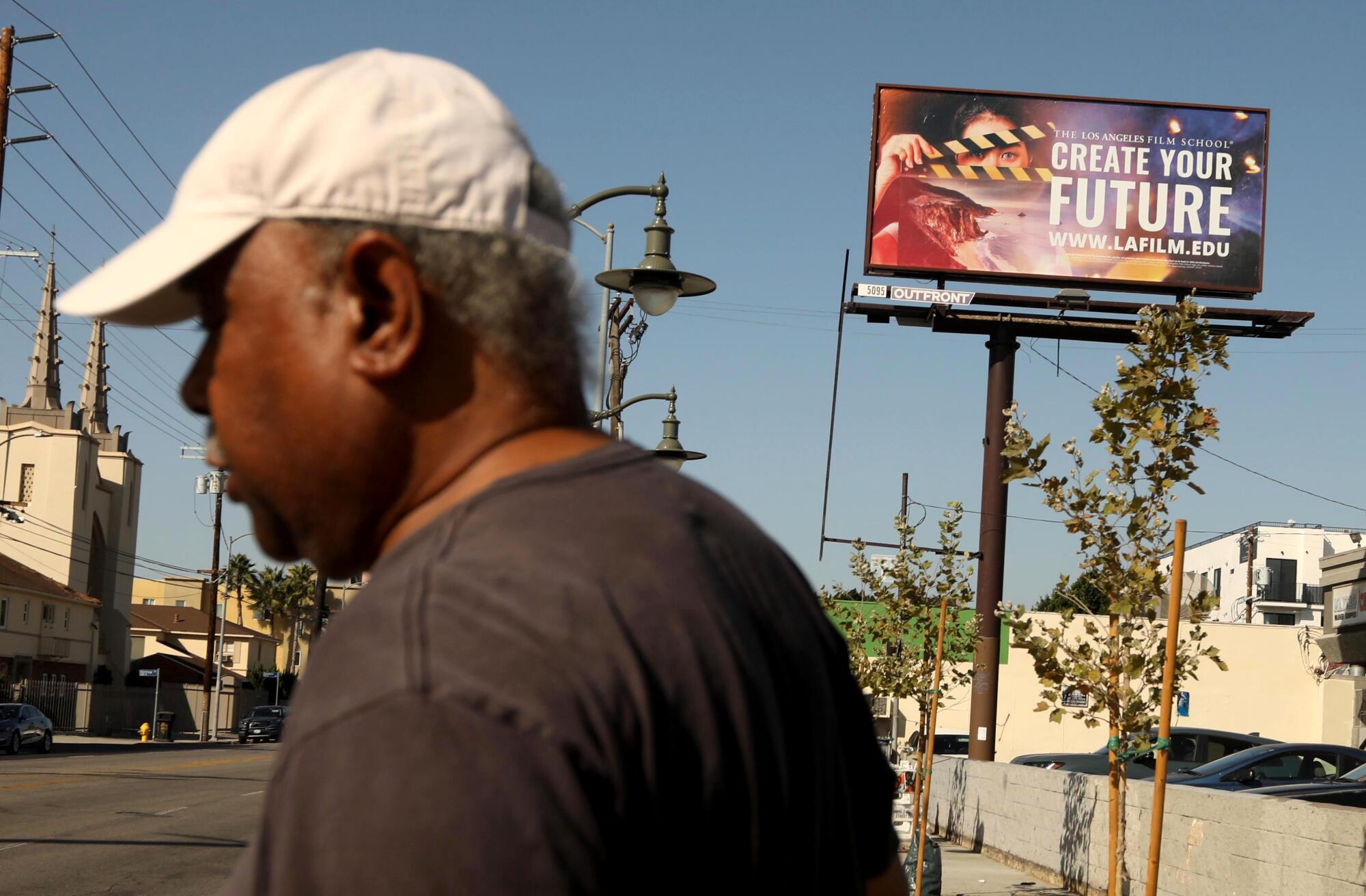 A man wearing a hat walks past a billboard with the message: "Create Your Future."