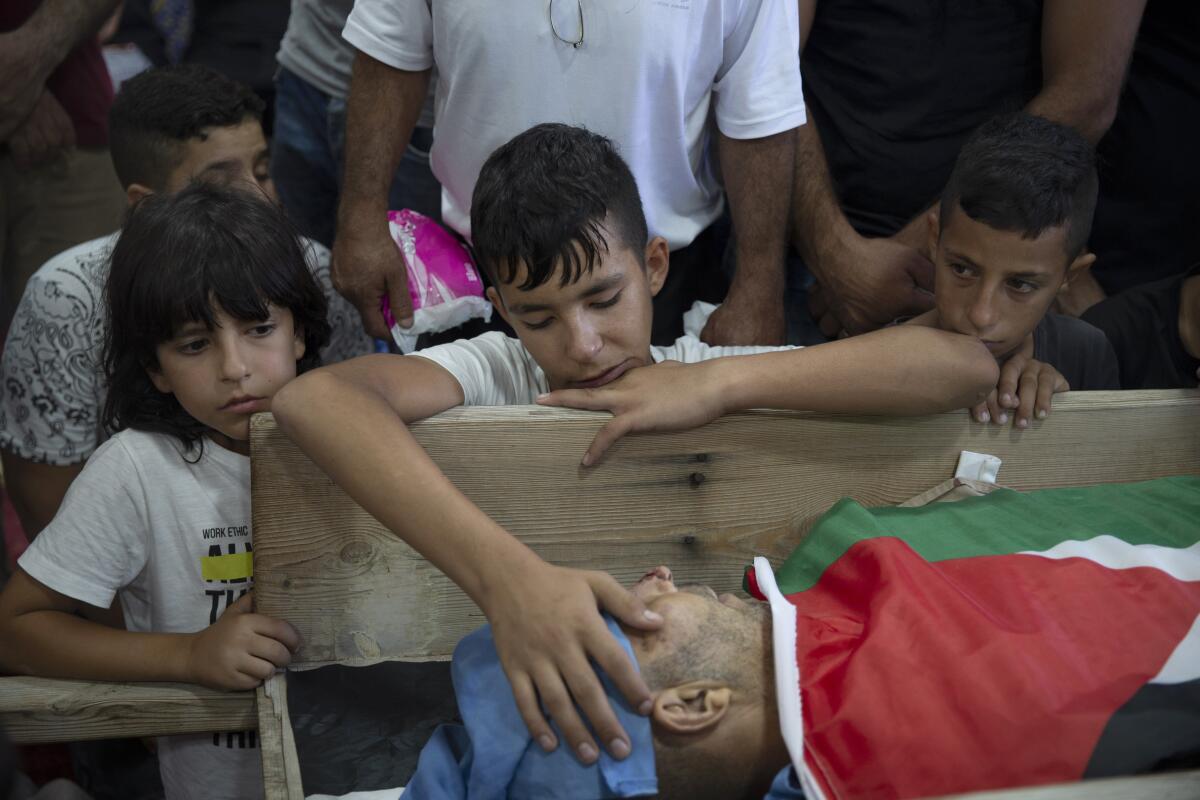 Palestinian Yousef Jadallah, places his hand on his father Raed Jadallah's body, who was killed by Israeli forces at the western entrance of his village while returning from work in the early hours of Wednesday morning, during his funeral, in the West Bank village of Beit Ur al-Tahta, Wednesday, Sep. 1, 2021. (AP Photo/Majdi Mohammed)