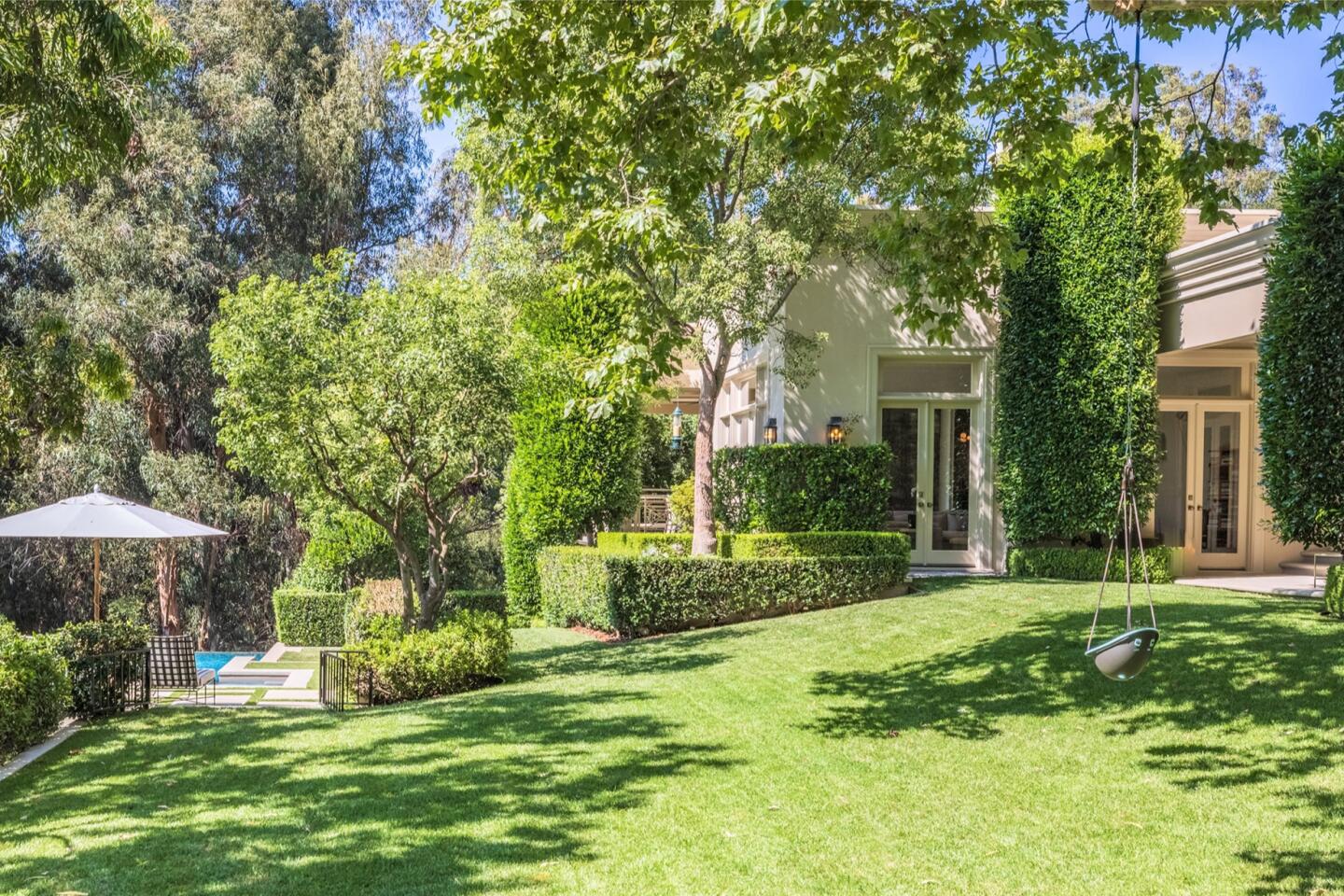 The backyard has a sloping lawn and trees.
