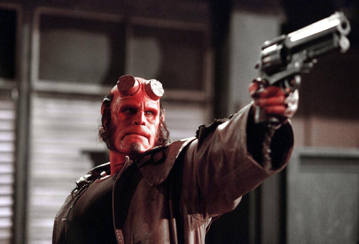 A big red demon in a leather trench coat points a large handgun.