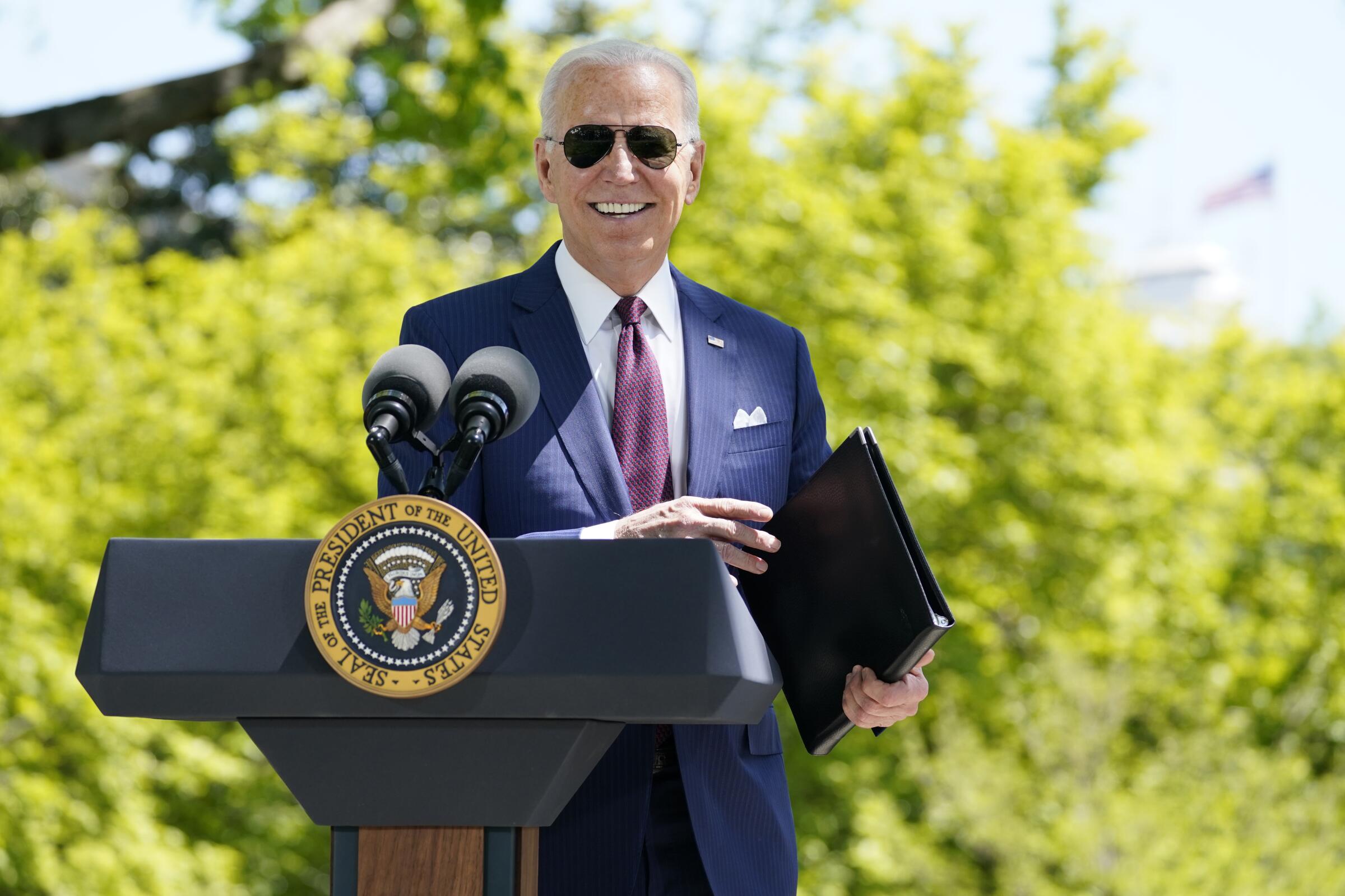 President Biden smiles as he stands behind a podium on the North Lawn of the White House 