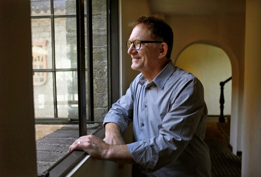 A man sits, looking out a window.