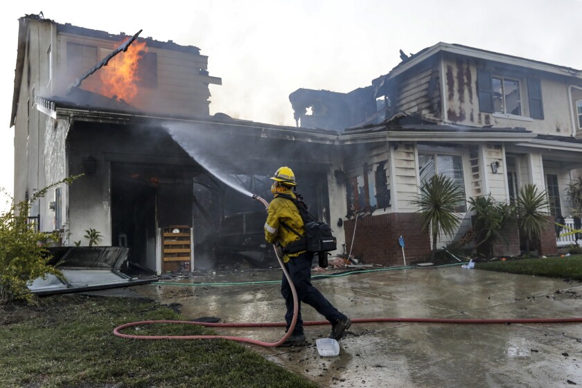 Firefighter douses a burning house in Santa Clarita during the Tick fire