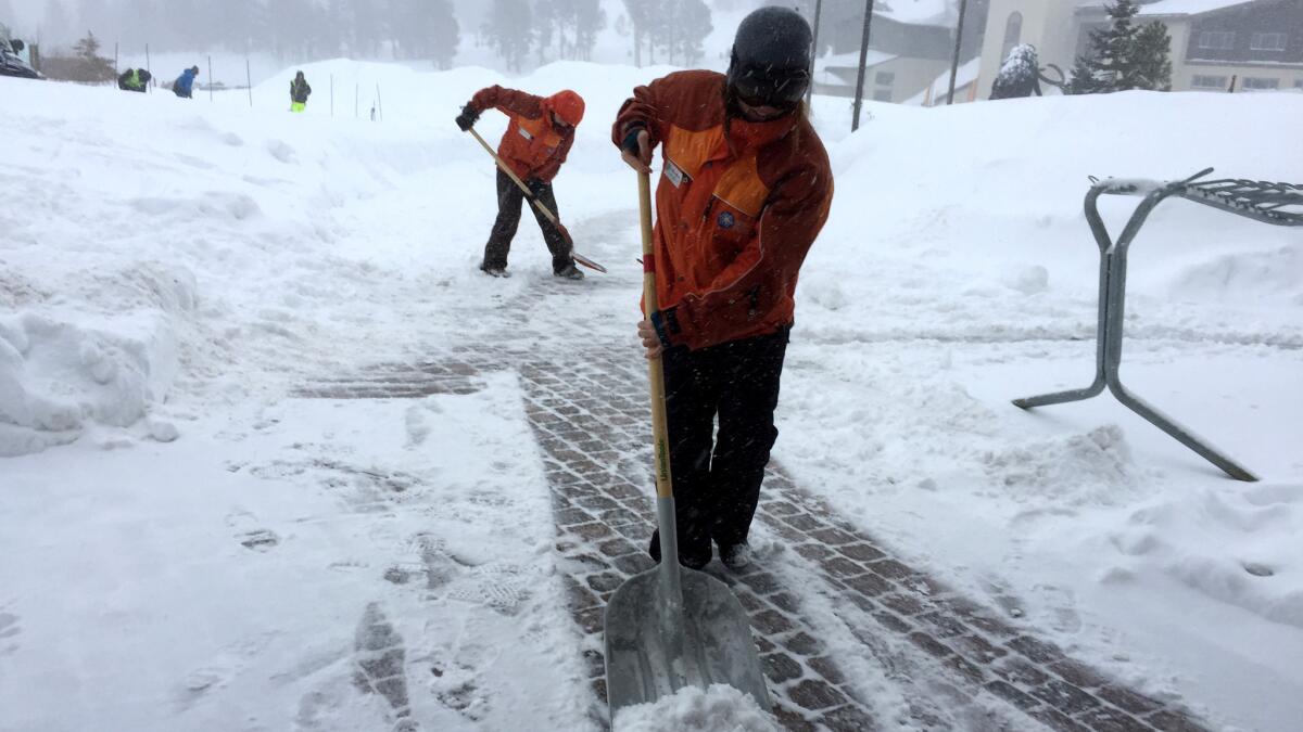 Mammoth Mountain employees clear paths as snow falls lightly Saturday morning.