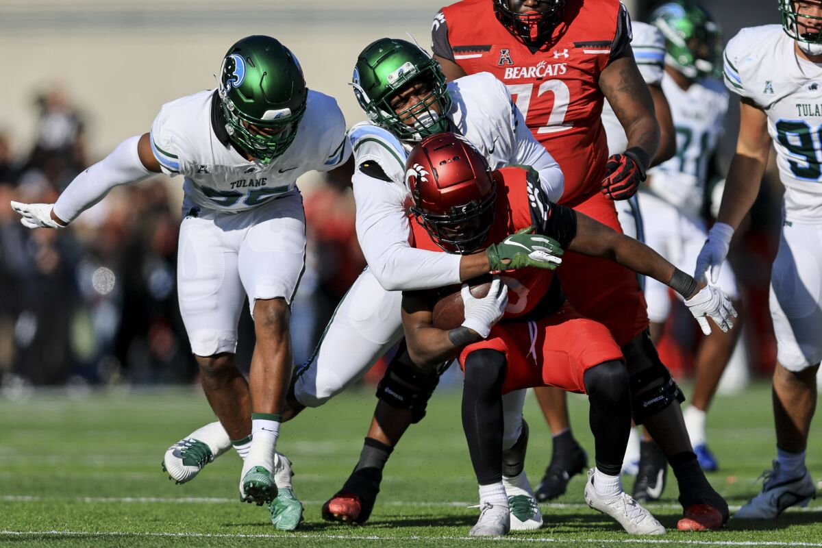 Cincinnati running back Charles McClelland, front, carries the ball as he is tackled by Tulane linebacker Keith Cooper Jr., back, while linebacker Jesus Machado, left, supports during the second half of an NCAA college football game, Friday, Nov. 25, 2022, in Cincinnati. (AP Photo/Aaron Doster)