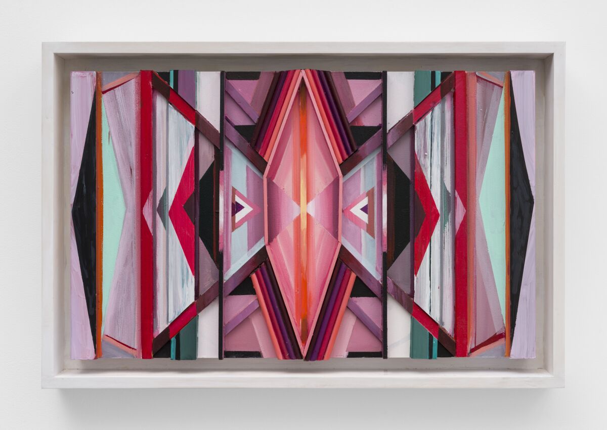 A geometric bas relief painting in shades of pink, red and aqua evokes female forms.