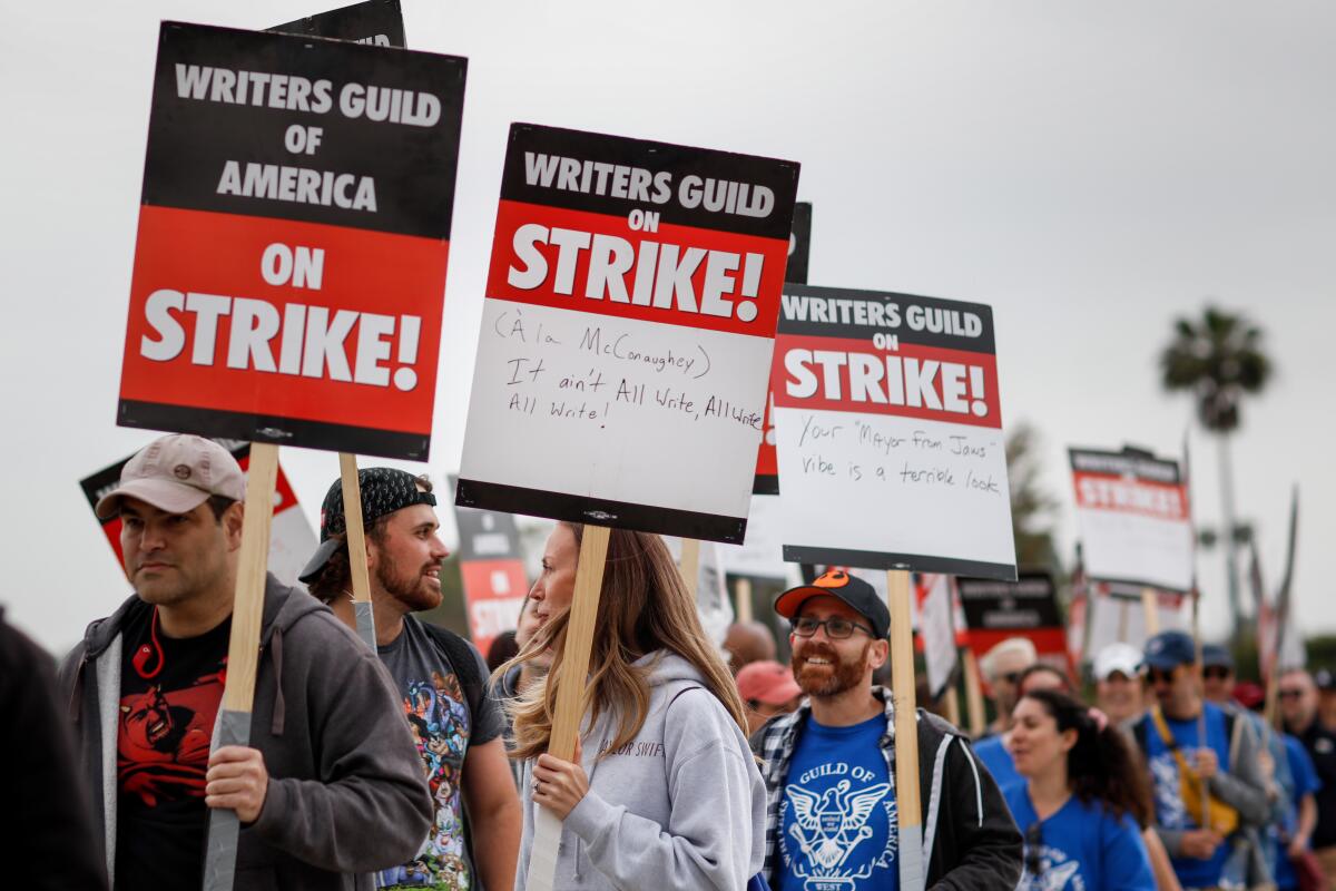 Supporters of the Writers Guild of America walk in a line carrying picket signs.
