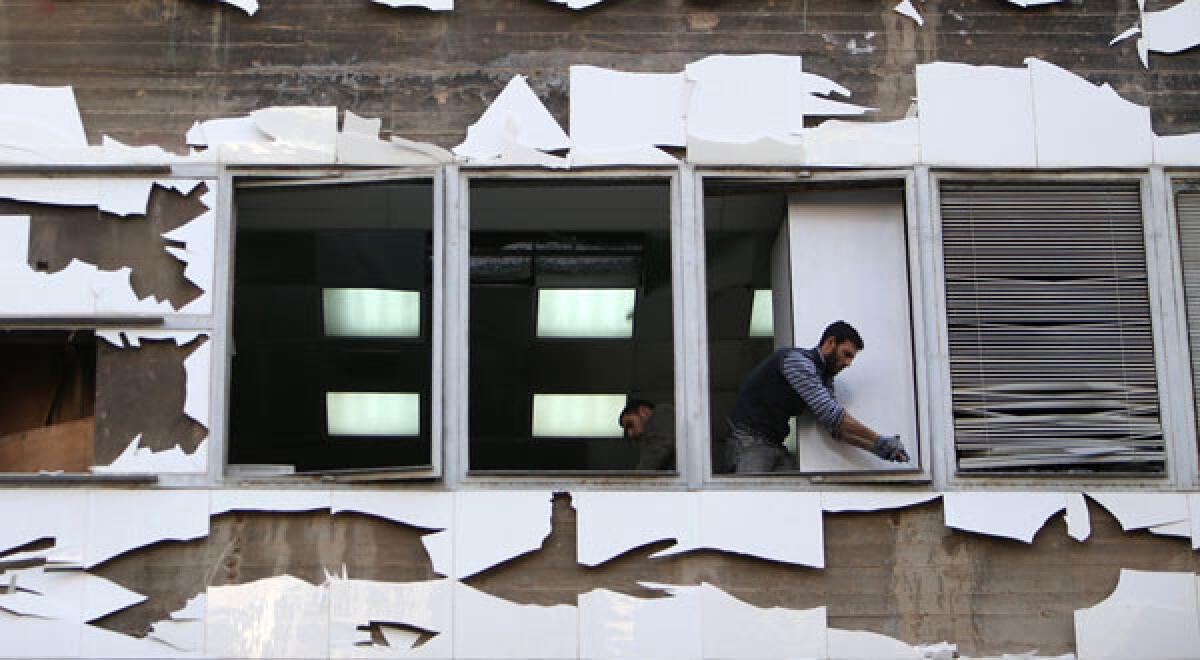 A worker cleans shattered glass from broken windows in a building near the scene of a massive explosion in Beirut.