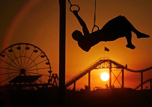 Beachgoer Paul Case swings on rings as the sun sets behind the Santa Monica Pier. Mild temperatures prevailed at the beach as hot summer weather continued to roast the rest of Southern California.