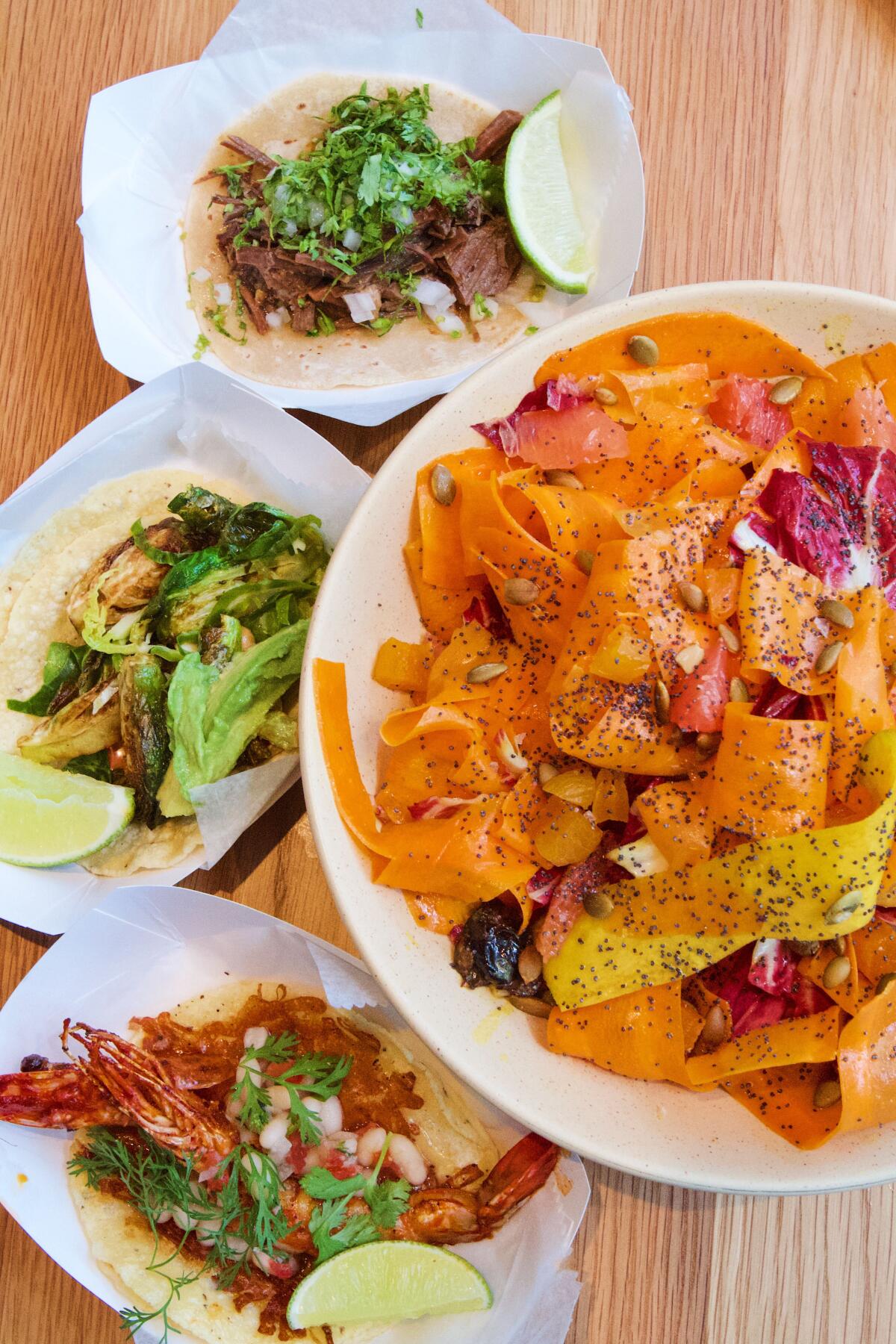 An overhead photo of a bowl of carrot salad and two kinds of tacos.