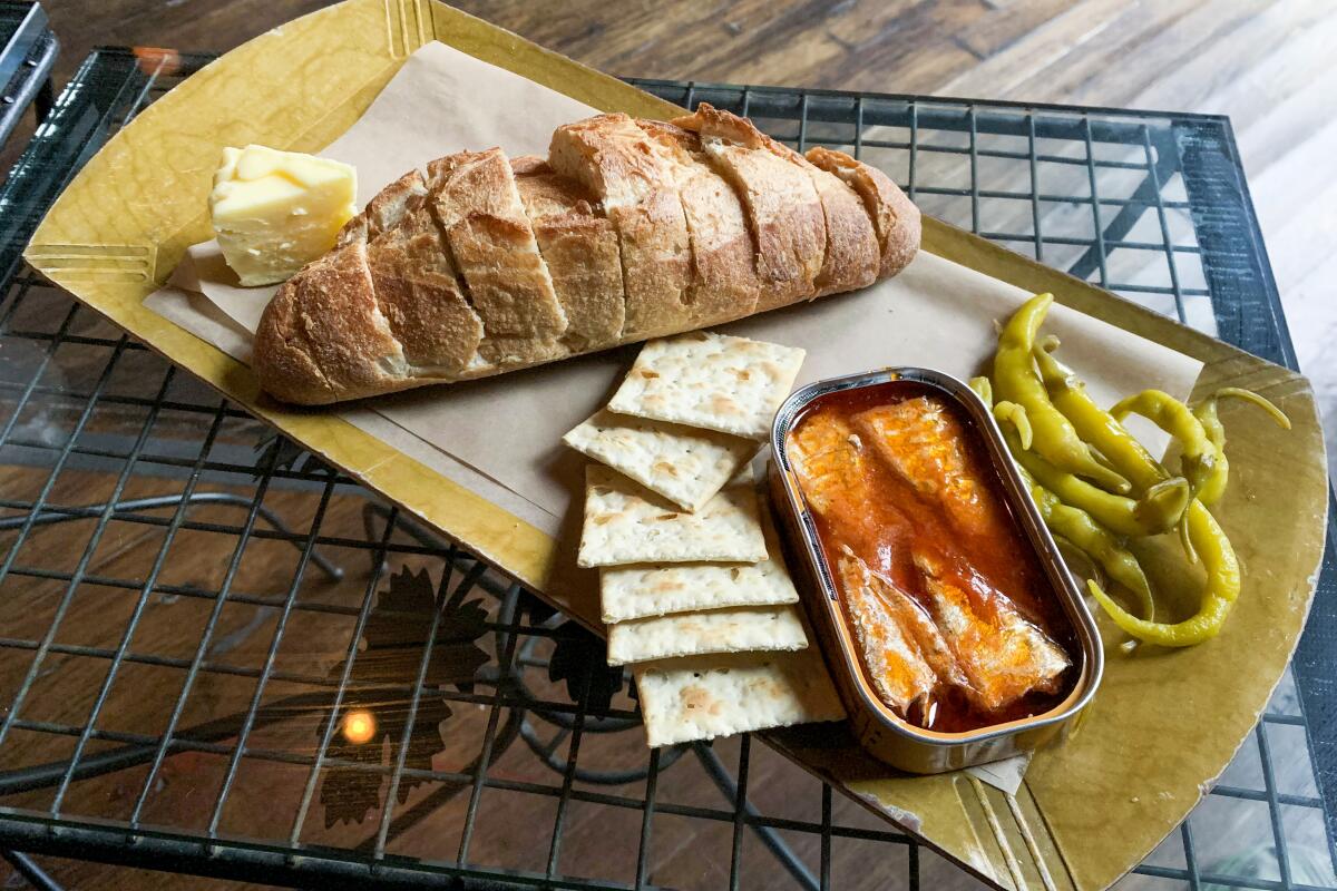 A tinned fish spread includes a baguette, crackers, pickled peppers and butter.