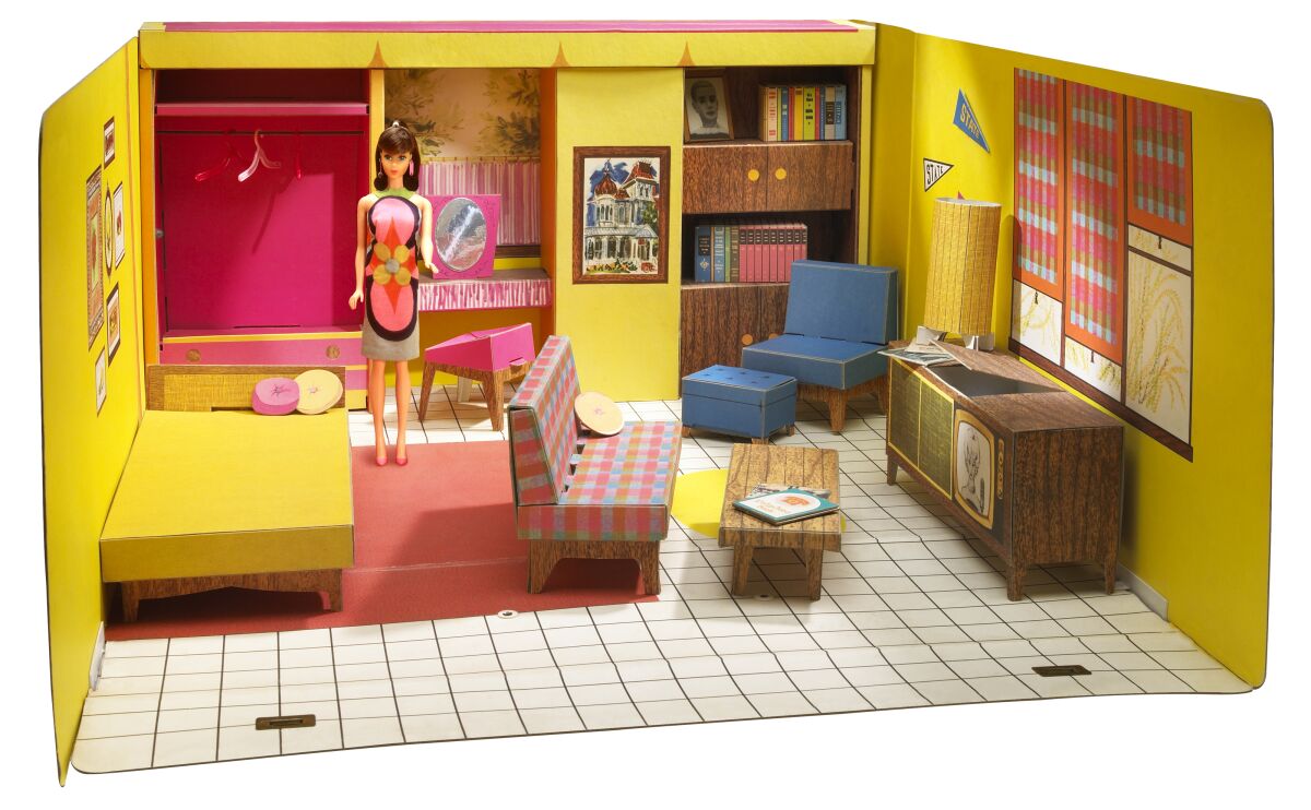 Barbie is shown standing in a Barbie dollhouse from the early '60s with bright yellow walls and a checked couch