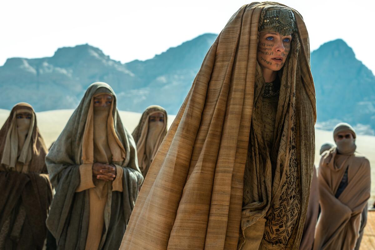 A group of women in the desert, in long draped ropes and head coverings