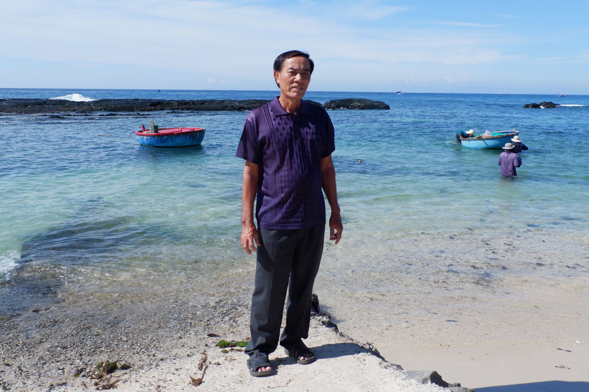 A man stands on the beach in front of a couple of small fishing boats