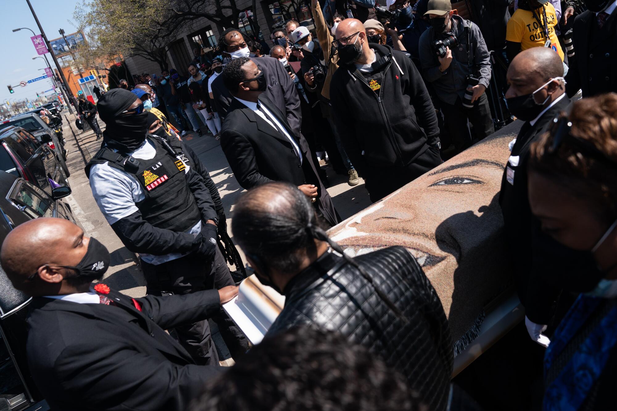 People in masks surround a casket bearing the image of a smiling young man
