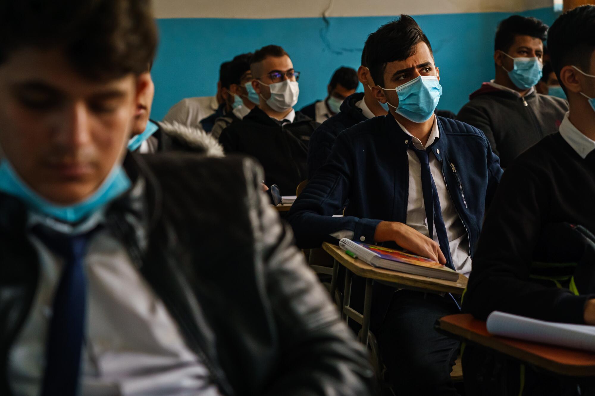 Male students, some wearing ties, sit at desks in a classroom 