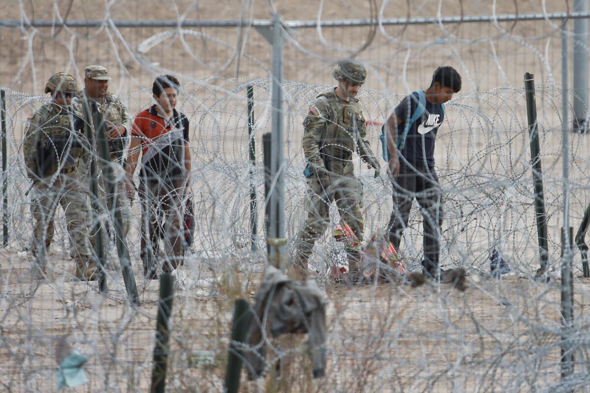 人们看到军队和移民一起走过铁丝网。