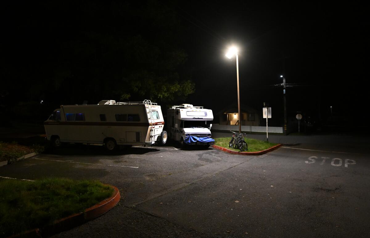 Two RVs are parked in a lot next to a light pole to which two bicycles have been locked.
