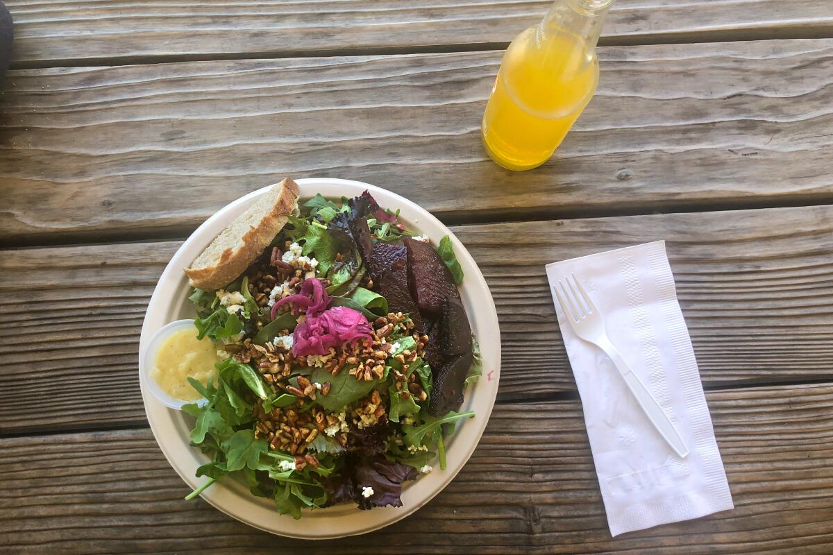 A salad and a glass bottle of an orange beverage on a wooden table.