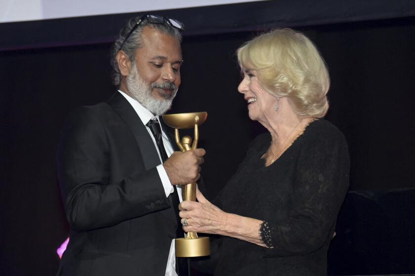 A man with gray hair and a beard and blond woman, both in formalwear, gripping a gold trophy