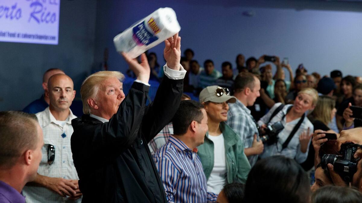 President Donald Trump tosses paper towels into a crowd like a basketball player taking a shot, at Calvary Chapel in Guaynabo, Puerto Rico on Oct. 3.