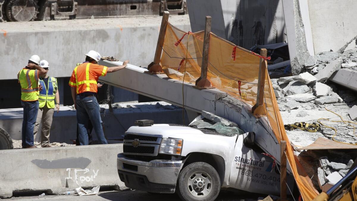 Workers stand next to a section of a collapsed pedestrian bridge on Friday near Florida International University in Miami.