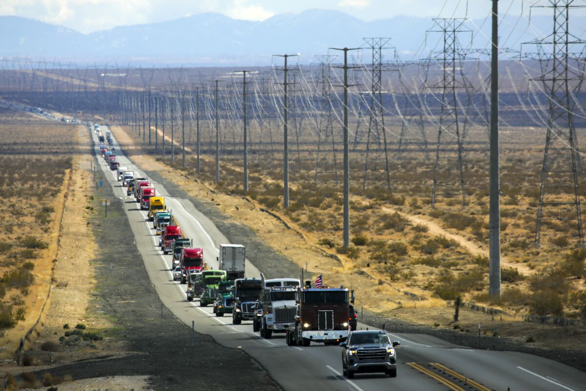 A long line of vehicles, including a lot of big rigs, moves along a rural highway.