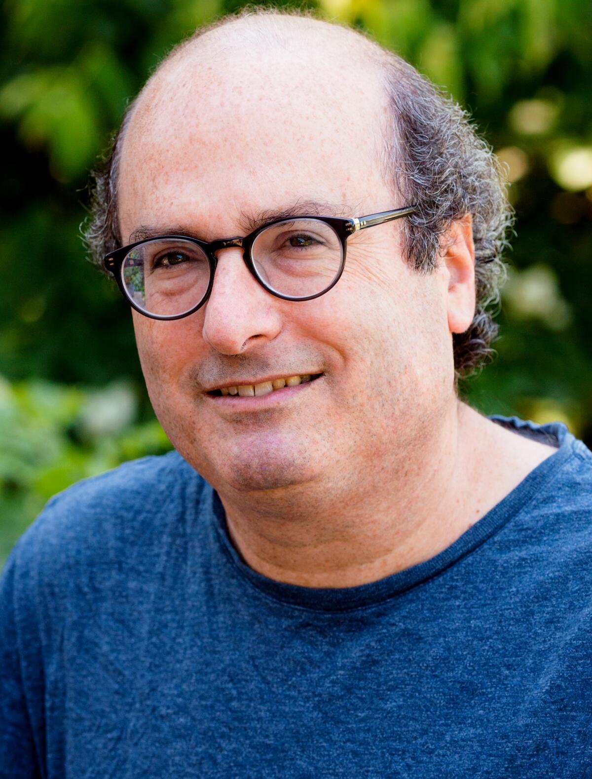A smiling, balding man in glasses and a blue shirt