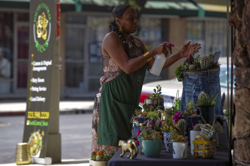 A woman uses a spray bottle to water a succulent arrangement that sits atop a table.