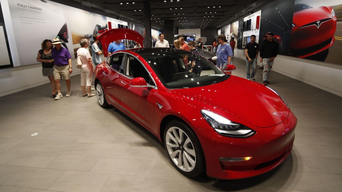 Prospective customers talk with sales associates as a Model 3 sits on display in a Tesla showroom in Denver in July.