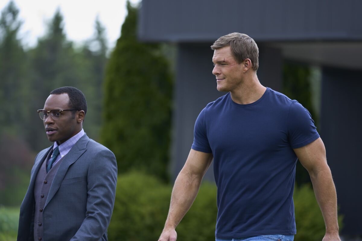 A shorter man in a suit next to a giant man in a tight T-shirt