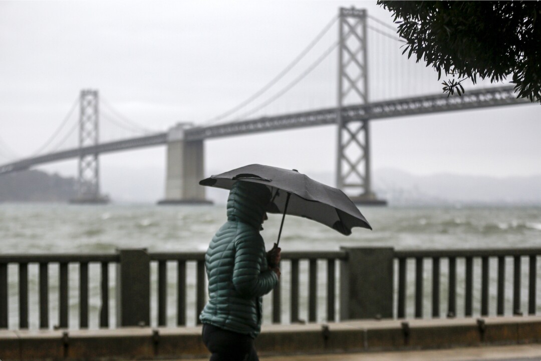 A person in a coat with an umbrella walks beside a rail overlooking a bridge over the water