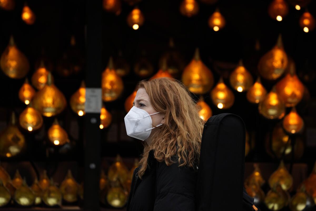 Una mujer utiliza una mascarilla mientras pasa entre luces navideñas en Londres, Inglaterra.