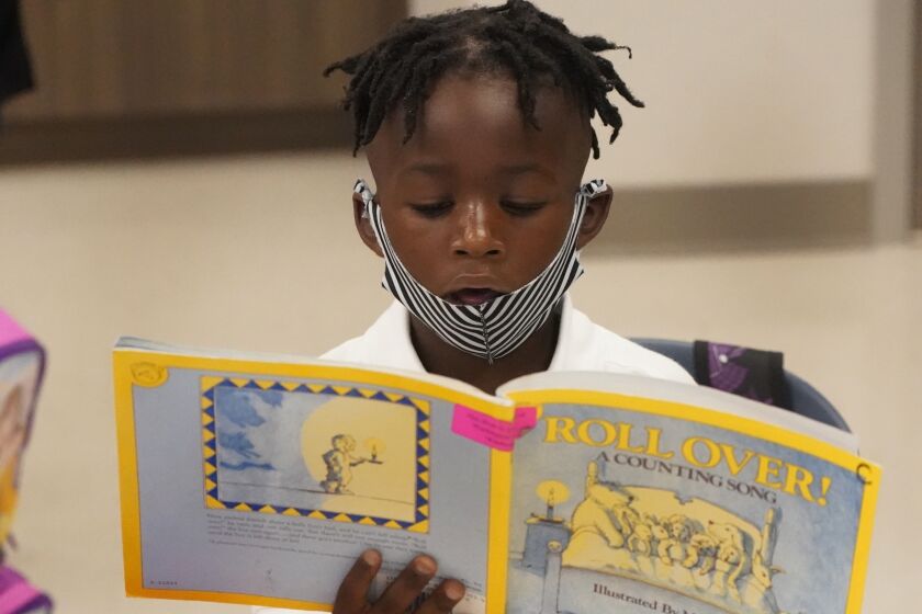 Kindergarten student Taiden Watkins reads a book, Tuesday, Aug. 10, 2021, during the first day of school at Washington Elementary School in Riviera Beach, Fla. (AP Photo/Wilfredo Lee)
