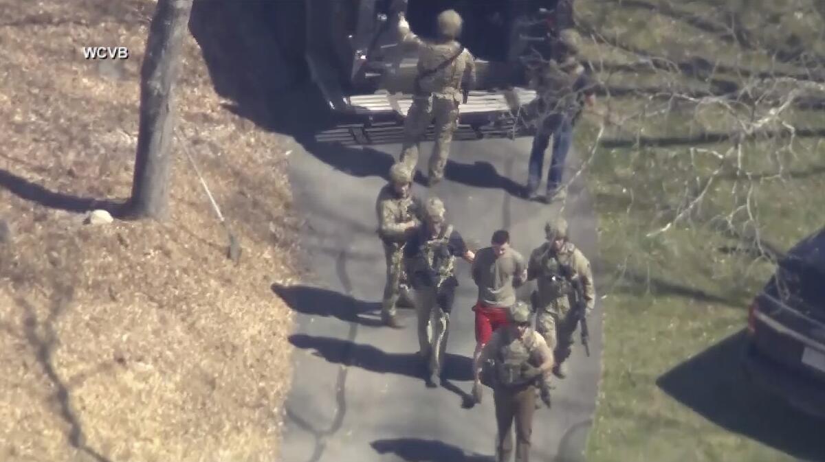 Jack Teixeira, in T-shirt and shorts, being taken into custody by armed tactical agents.