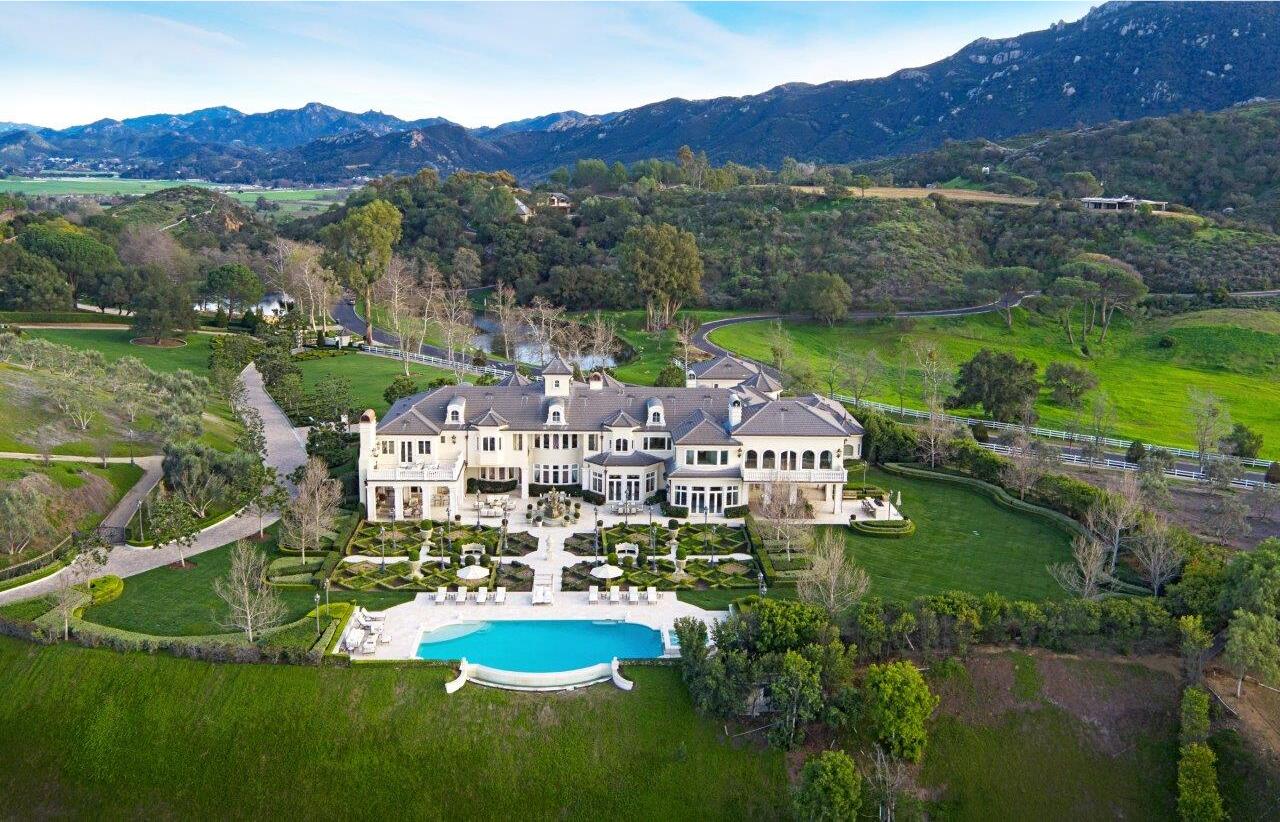An aerial view of the back of the mansion, green lawns, hills and mountains.