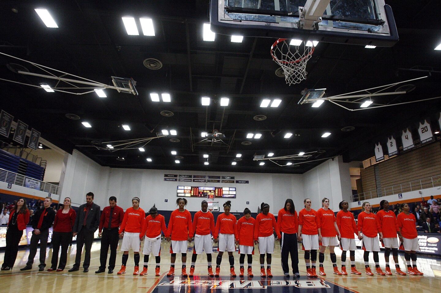 Members of the Cal State Fullerton women's basketball team join hands for a moment of silence to honor slain assistant coach Monica Quan before a home game against UC Irvine.