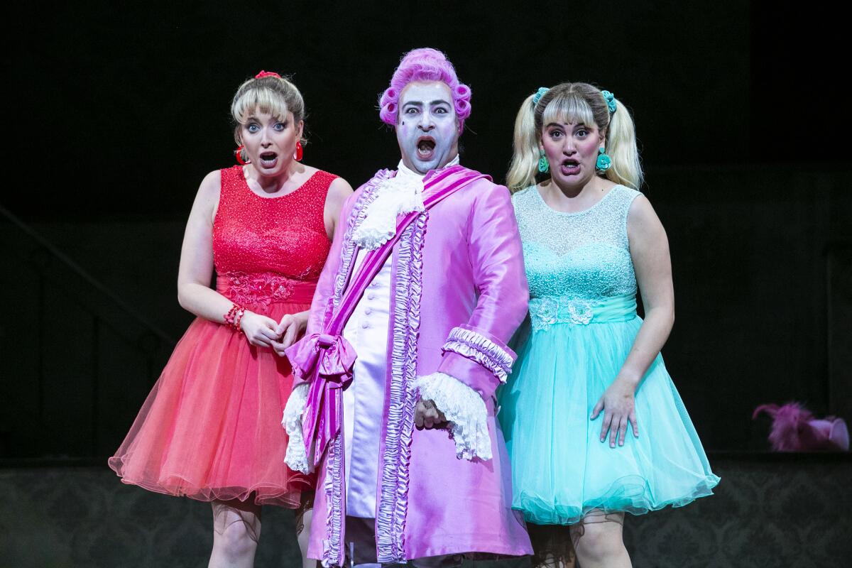 A woman in a red dress, left, a man in a bright purple jacket and purple hair, middle and a woman in a teal dress all gasp