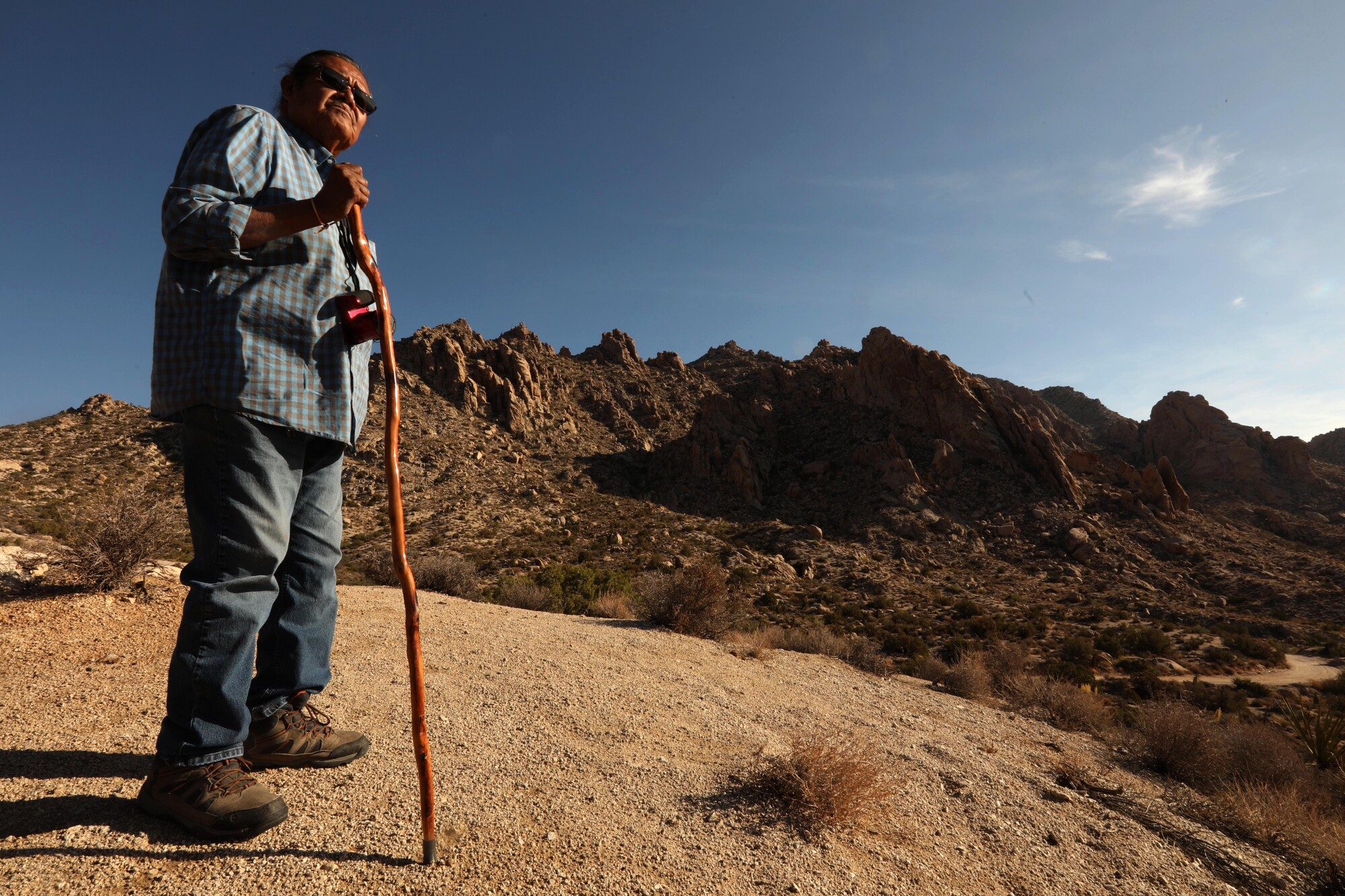 A man leans on a walking stick in the desert.