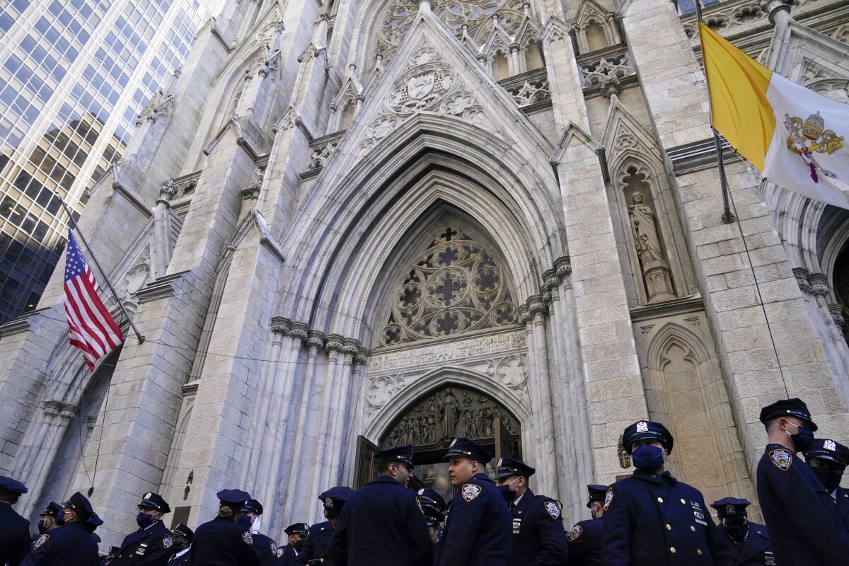 NYPD officers stand outside on Fifth Avenue before the casket of New York City Police Officer Wilbert Mora is delivered to St. Patrick's Cathedral for his wake, Tuesday, Feb. 1, 2022, in New York. Mora and Officer Jason Rivera were fatally wounded when a gunman ambushed them in an apartment as they responded to a family dispute. (AP Photo/John Minchillo)