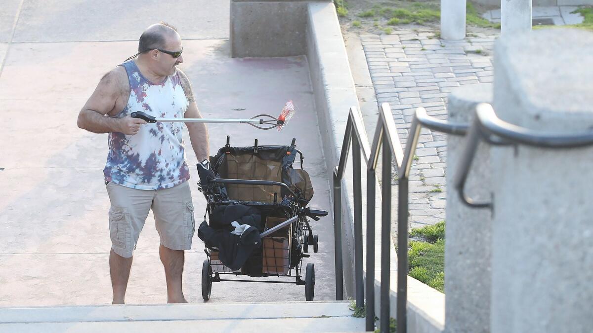 David Hubbard collects trash on the stairs near the Huntington Beach Pier. For the past year, the Surf City resident has picked up 30 to 40 pounds of trash nearly every day while walking along a stretch of Pacific Coast Highway.