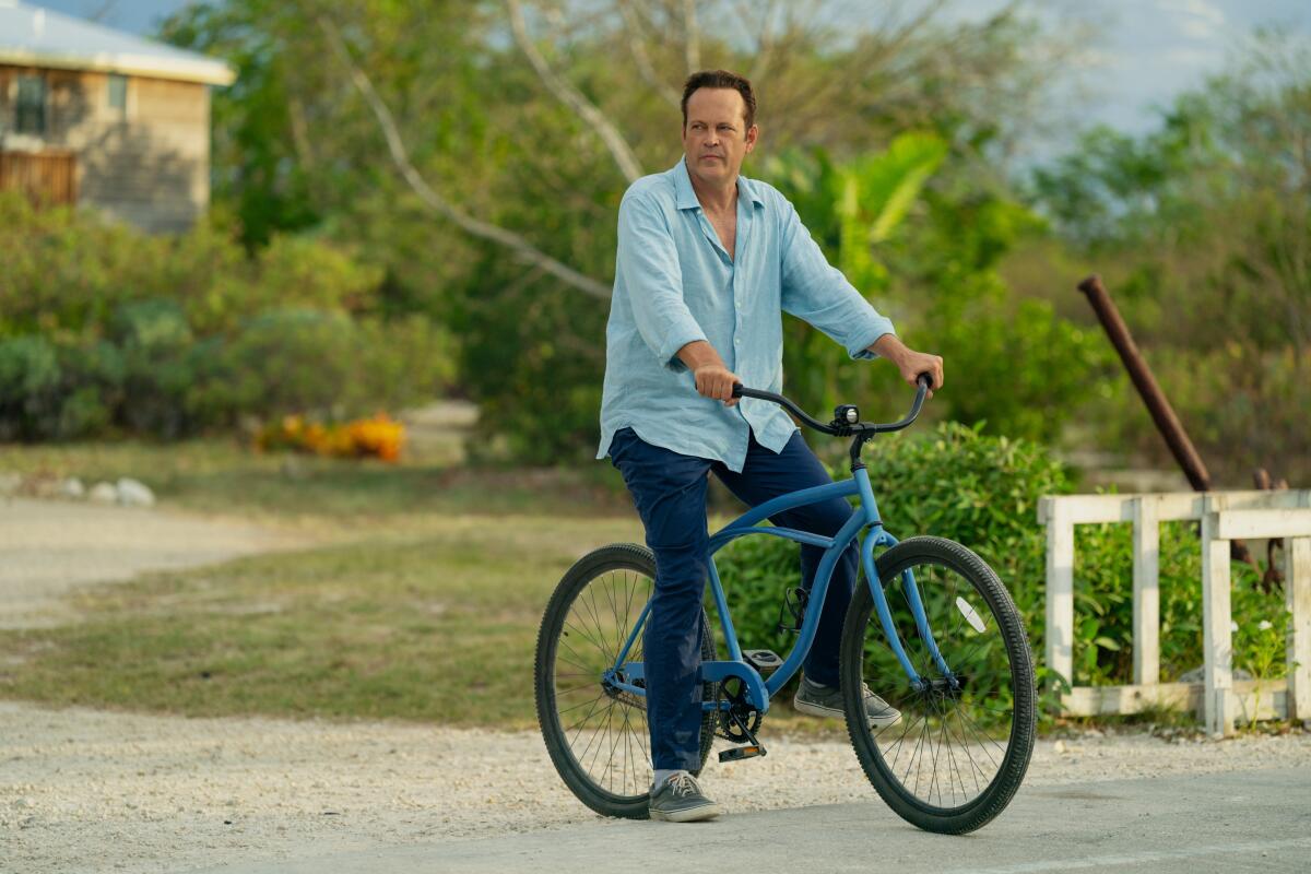 A man in a blue shirt and jeans riding a blue bike.