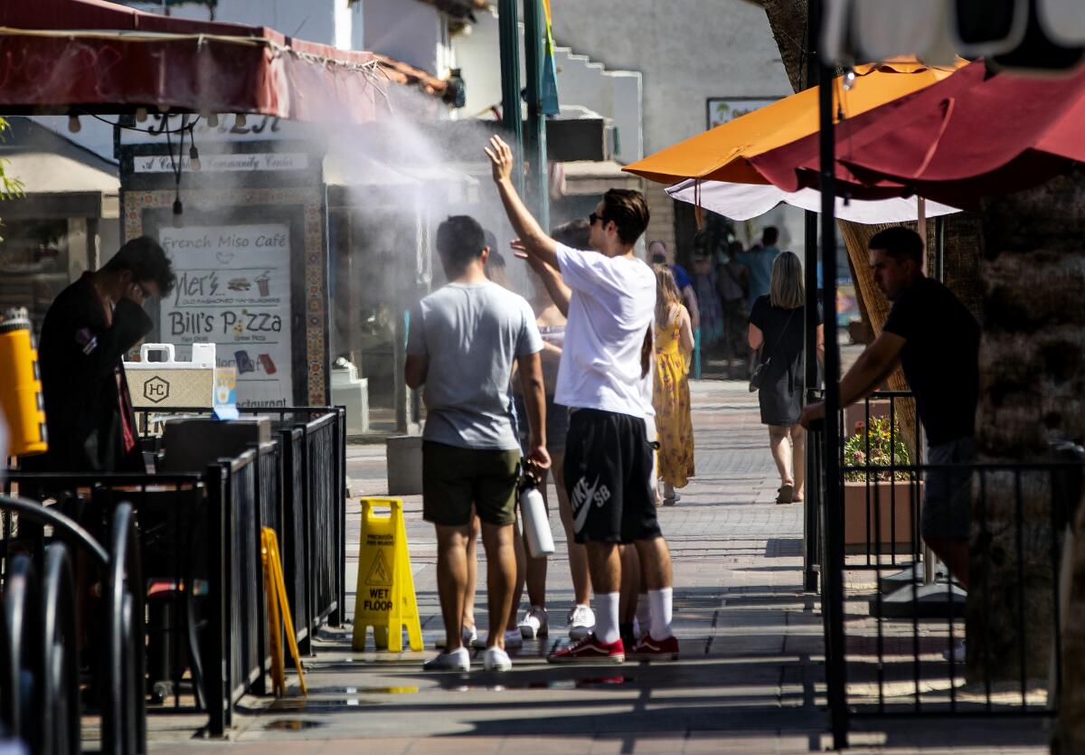 Several people, one holding a water bottle, stand next to an awning and beneath a spray of water.