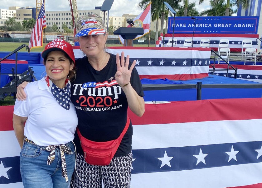Two women pose in front of an outdoor stage decorated with red, white and blue bunting