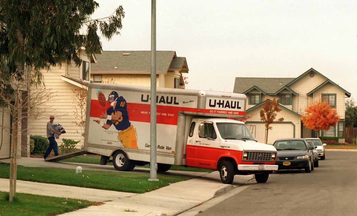 A man carries items up a ramp into a U-Haul truck parked in a driveway.