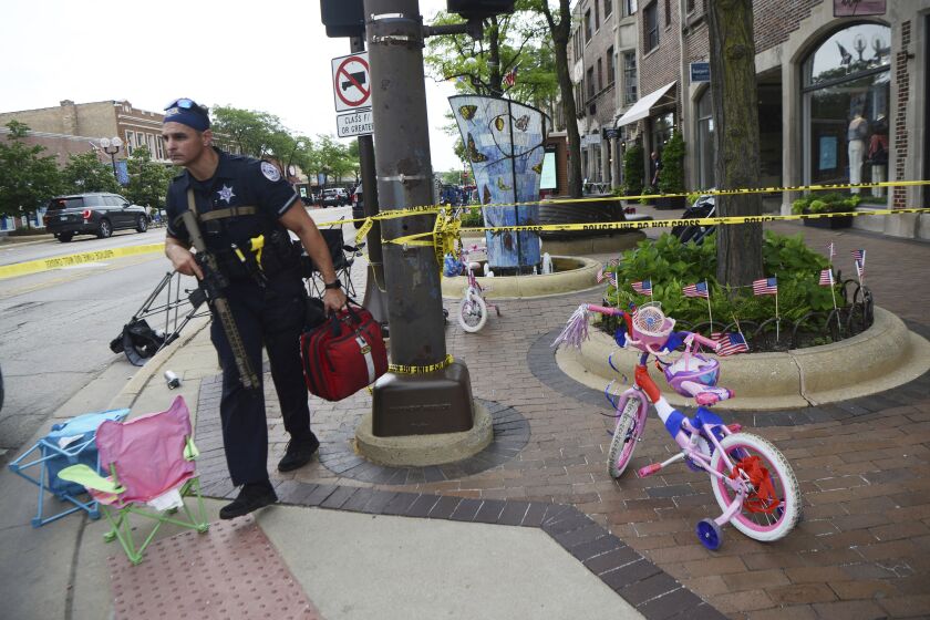 A police officer walks past a child's bicycle that was left along the parade route a block away from the scene of a shooting involving multiple victims that took place at the Highland Park, Ill., Fourth of July parade Monday, July 4, 2022. (Joe Lewnard//Daily Herald via AP)