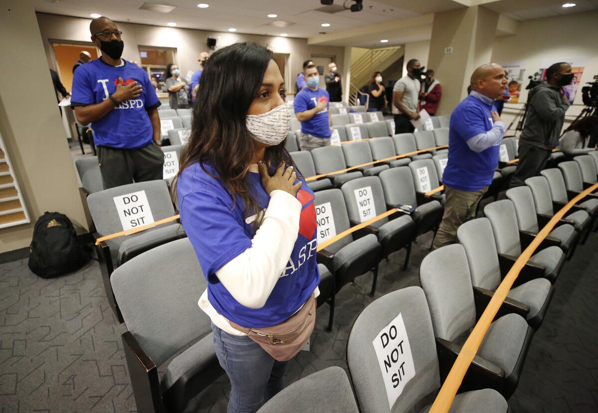 People with shirts that say I heart LASPD stand with their right hands over their hearts at a meeting